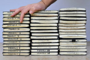 A stack of Moleskine notebooks with a hand resting on top